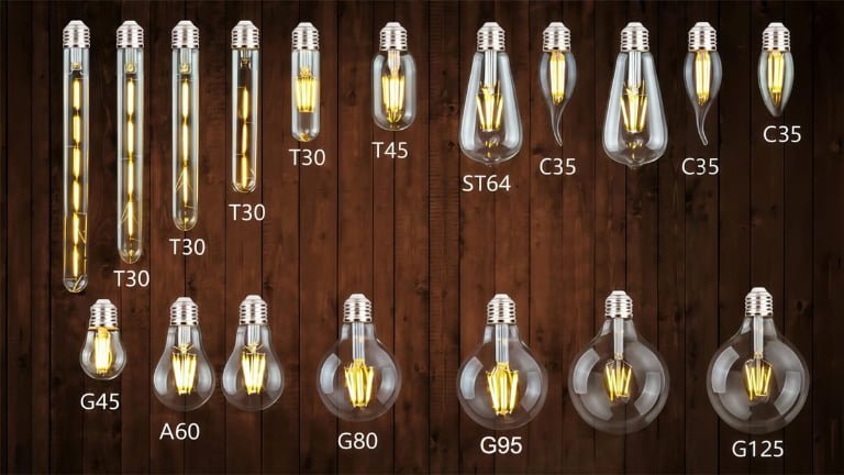 Assortment of vintage LED filament light bulbs on a dark wooden background. The image displays various shapes labeled with their codes: T30, T45 (Tube), ST64, C35 (Candle), A60, and Globe series G45, G80, G95, G125.