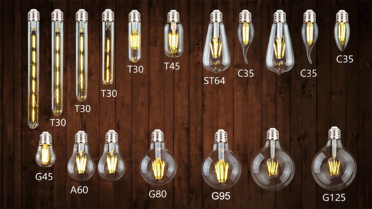 Assortment of vintage LED filament light bulbs on a dark wooden background. The image displays various shapes labeled with their codes: T30, T45 (Tube), ST64, C35 (Candle), A60, and Globe series G45, G80, G95, G125.